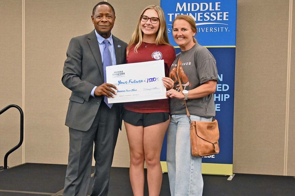 Middle Tennessee State University President Sidney A. McPhee, at left, presents a $1,500 scholarship to Sydney Bunner, center, a senior at Westminister Christian Academy in Huntsville, Ala., along with her mother, Beth Bunner, on stage during the True Blue Tour student recruitment reception held Wednesday, Oct. 14, at The Westin Huntsville. The high schooler is wearing a shirt she received after attending the Forensic Institute for Research and Education CSI: MTSU Camp over the summer at the Murfreesboro, Tenn., campus, where she learned more about the career field that is drawing her to MTSU’s forensics program. (MTSU photo by Nancy DeGennaro)