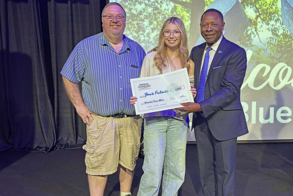 Middle Tennessee State University President Sidney A. McPhee, right, presents a scholarship to L&N STEM Academy senior Melanie Milliken, center, and her father, Scott Milliken, at the True Blue Tour student recruitment stop held at Bridgewater Place in Knoxville, Tenn., on Sept. 30, 2026. Eight students were awarded a total of $8,500 in scholarships at the evening reception on Sept. 30, 2026. (MTSU photo by Nancy DeGennaro)