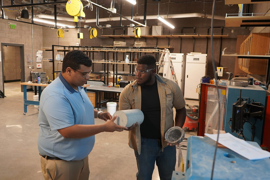 Elijah Echols, right, lab assistant for the School of Concrete and Construction Management at Middle Tennessee State University, shows Lucas Daggs, a construction management major, how to set up a test cylinder of concrete in a compression machine on campus in Murfreesboro, Tenn. (MTSU photo by Robin E. Lee)