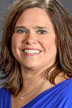 A woman with light skin and brown hair smiles at the camera.
